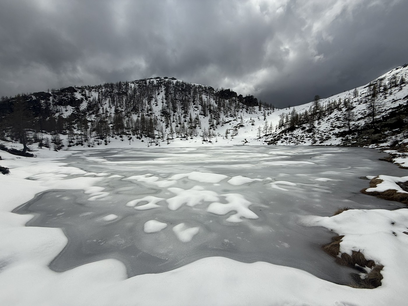 Frozen alpine lake at Alpe di Salei, surrounded by snow-covered slopes beneath dark clouds