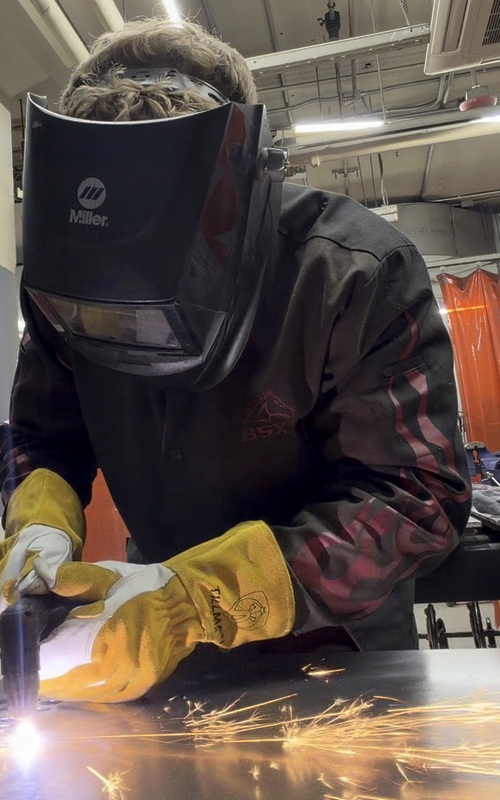 Kevin Boehm plasma cutting steel, with his protective helmet down and sparks streaming from the torch