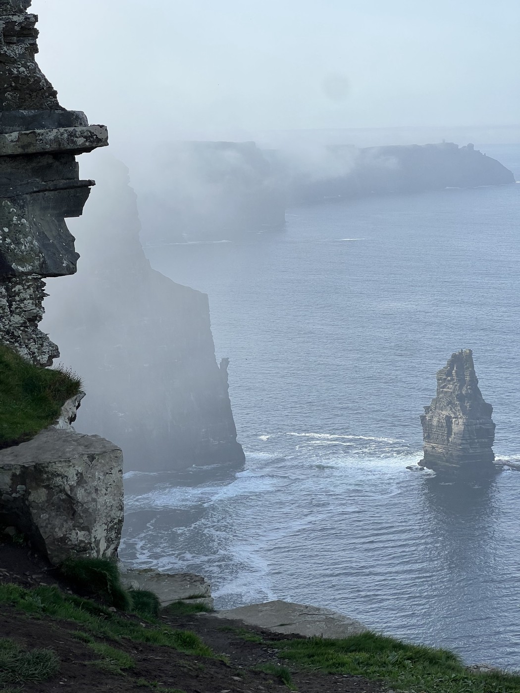 Sheer cliffs and a sea stack emerging through mist above the Atlantic at the Cliffs of Moher